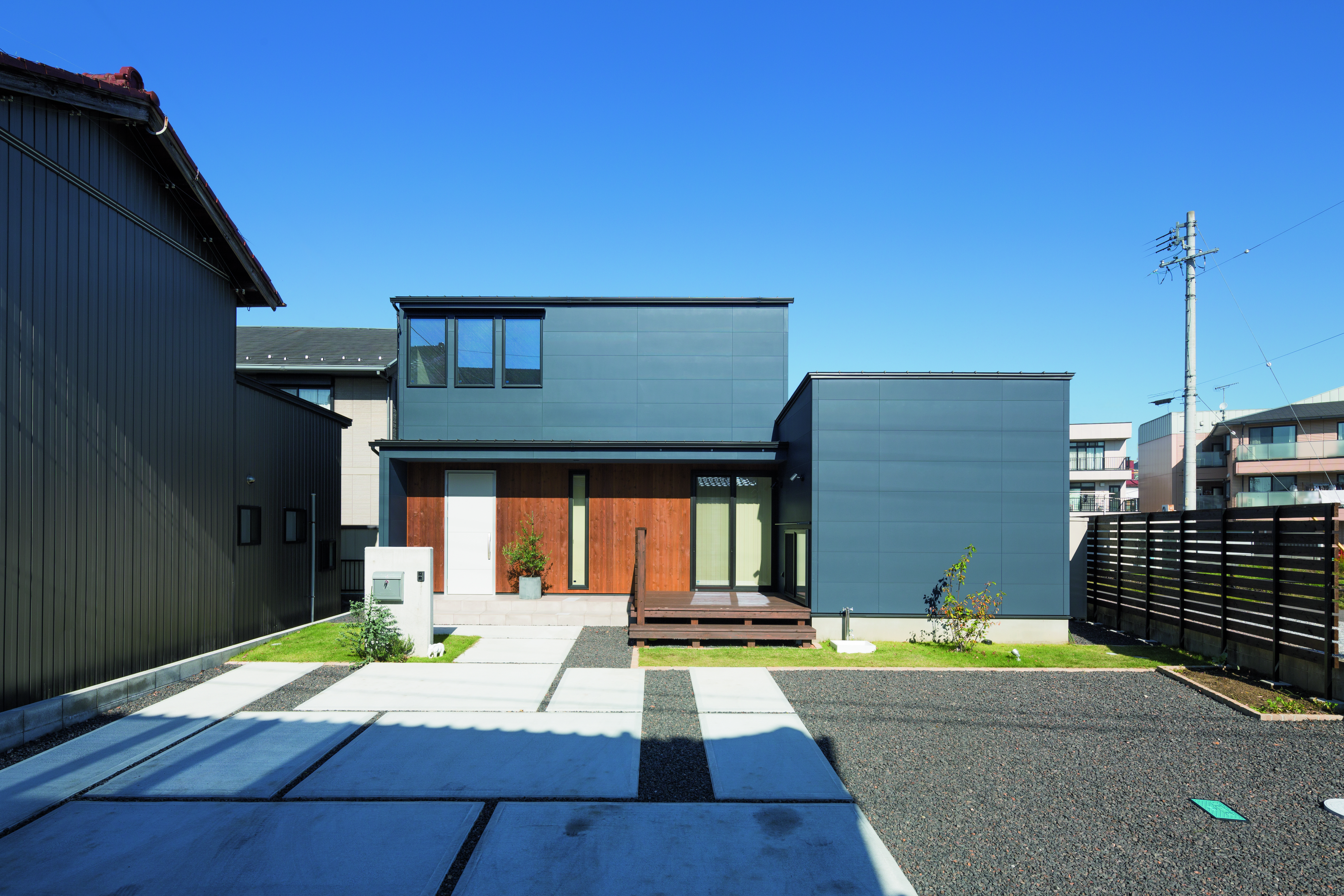 Front-facing view of a home with navy and wooden siding and a concrete-tiled and gravel driveway