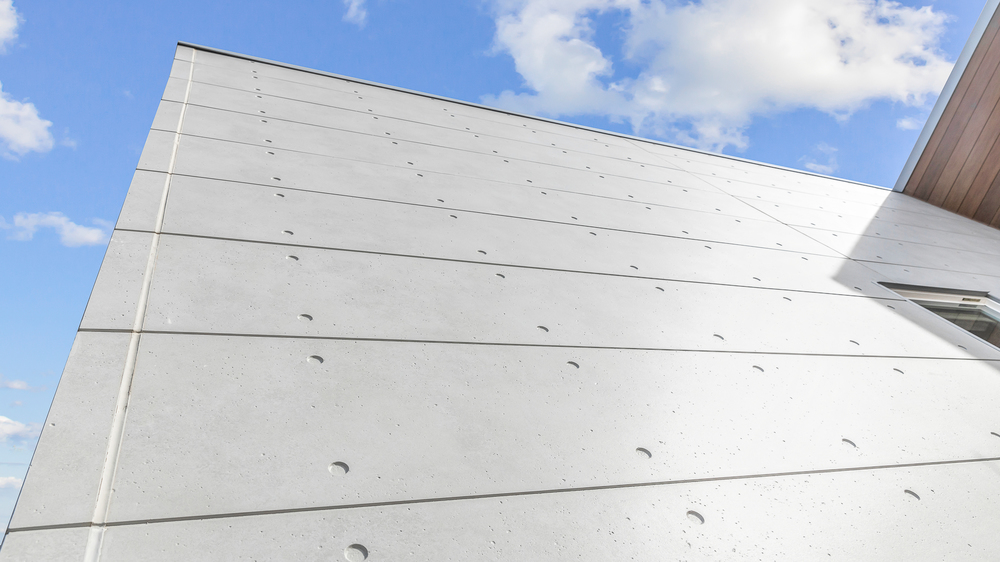 A close-up of fiber cement cladding on a building exterior with a blue sky in the background.