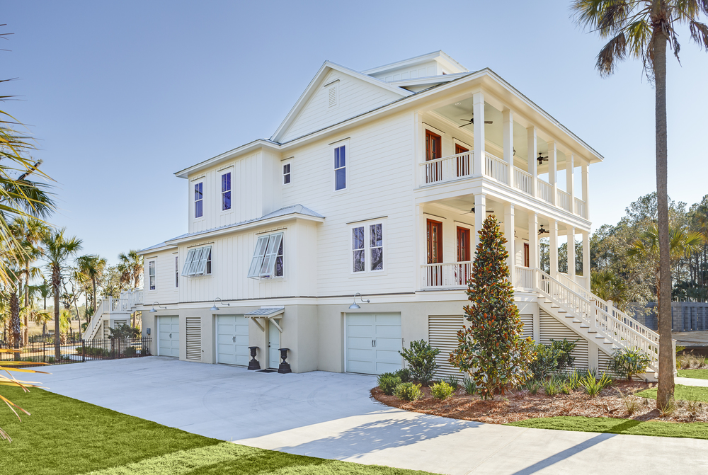 A large white house is elevated on risers. There are white steps leading up to a porch and the front door. Various plants surround the front.