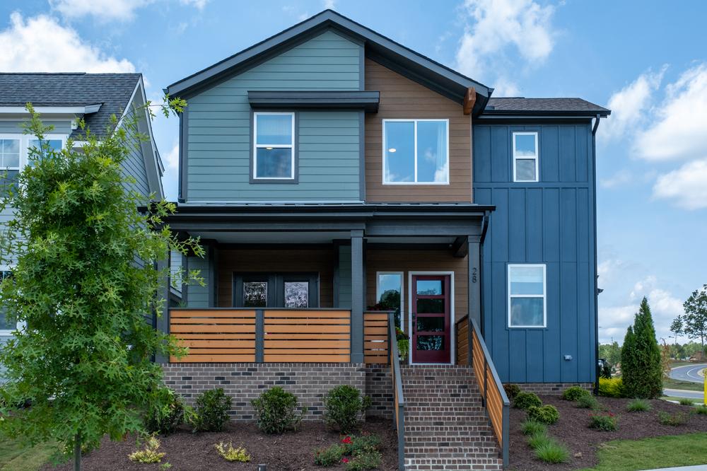 A two-story home featuring both horizontal and vertical siding in blue and brown tones. There are brick steps leading up to the front porch.