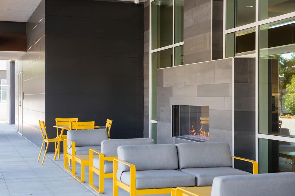Homewood Suites Hotel using gray Nichiha fiber cement cladding panels for an outdoor fireplace area. There are yellow tables and benches out front for a pop of color.