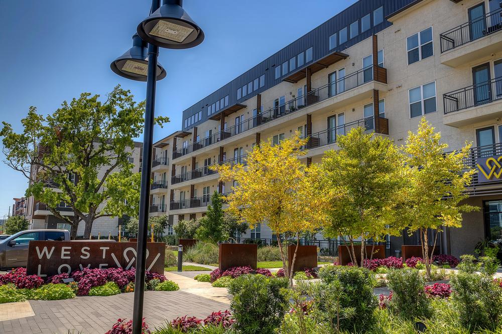 10 West Love apartments in Dallas with Nichiha’s fiber cement cladding and many trees, flowers and bushes in front of the building.