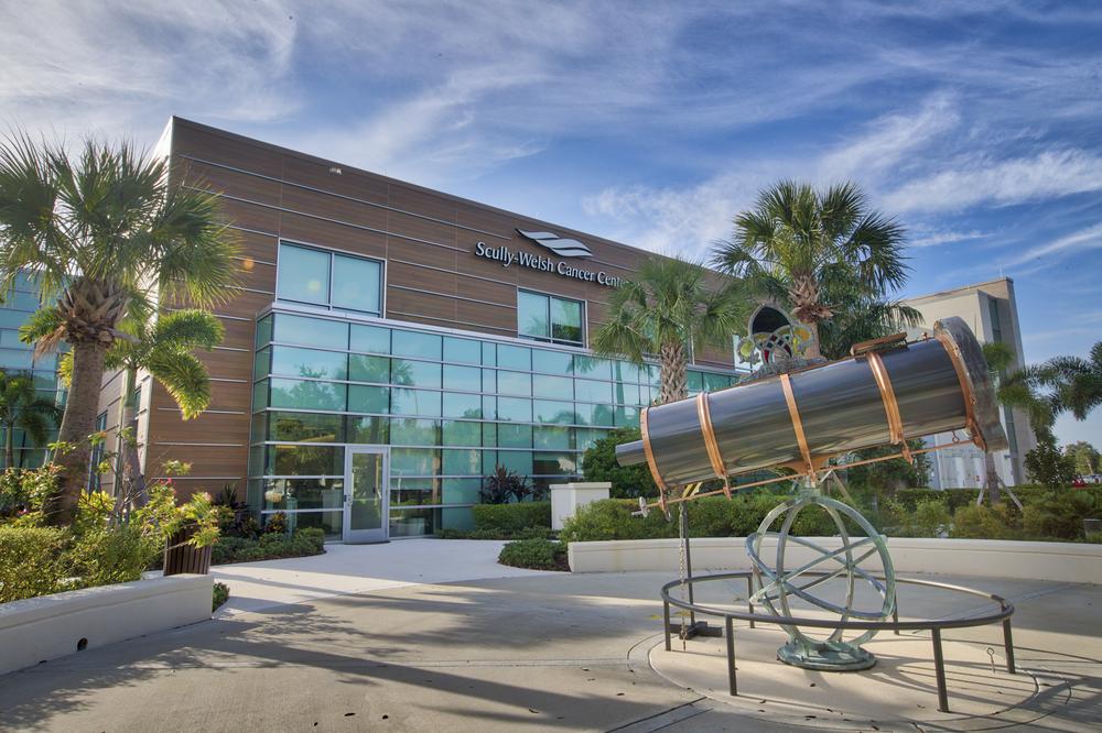 A shot of the Scully Welsh Cancer Center in Florida utilizing Nichiha&rsquo;s VintageWood fiber cement siding in Cedar. There are palm trees around it, a lot of windows on the building and a large telescope sculpture propped in front.