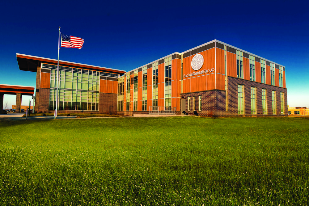 A photo of Racine Dental Group building utilizing Nichiha&rsquo;s VintageWood fiber cement cladding in Cedar with a grass field in front and an American flag blowing in the wind.