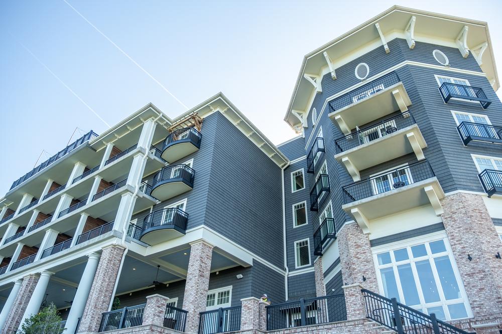 An upwards view of blue shake fiber cement siding, white and black iron balconies and light brick pillars.
