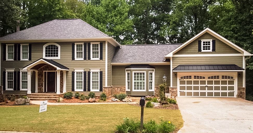 A front view of a traditional modern house with brown-toned fiber cement siding, white-framed windows and black shutters.