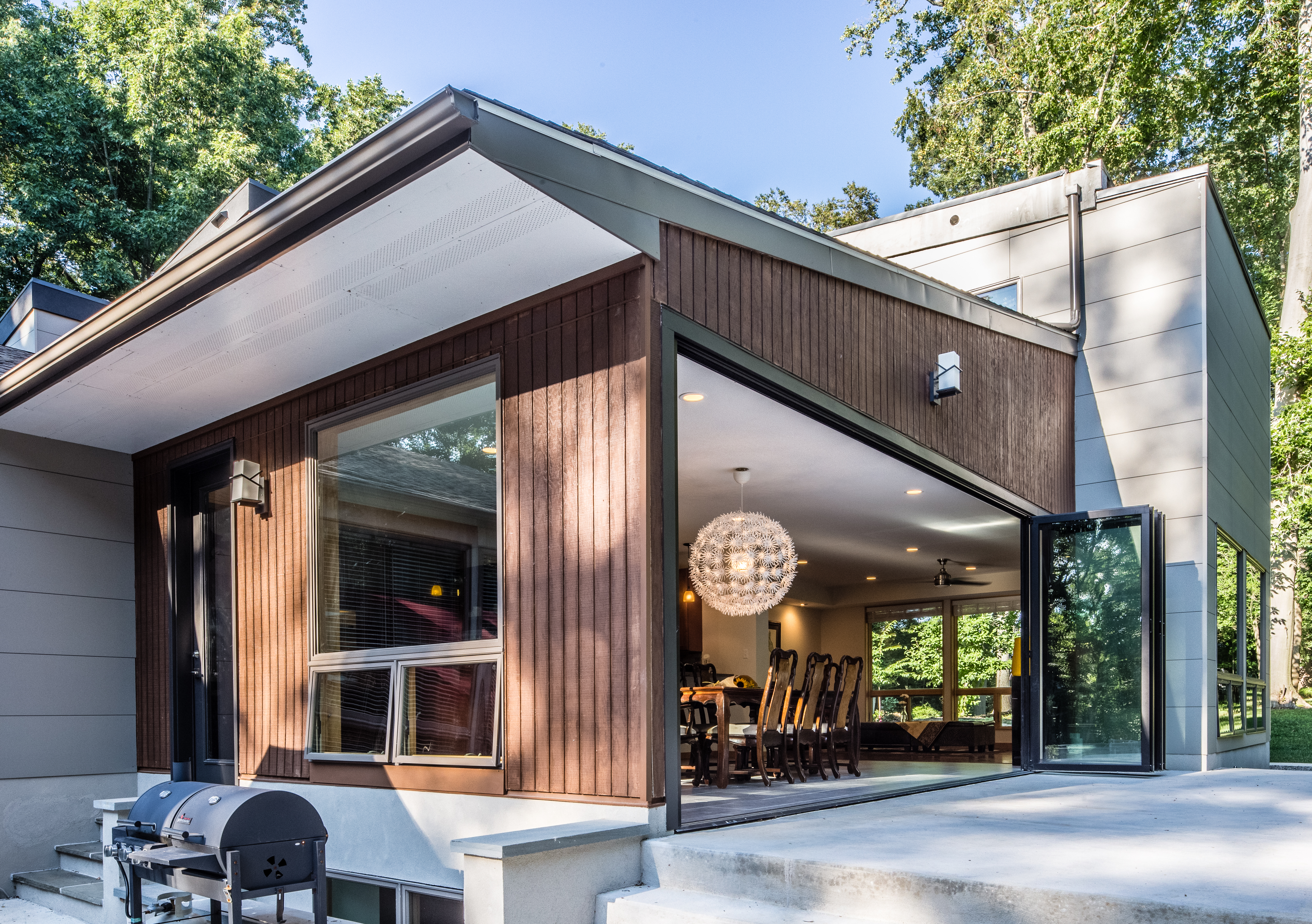 Brown and grey home with a wall that opens from a living room to a large deck area.