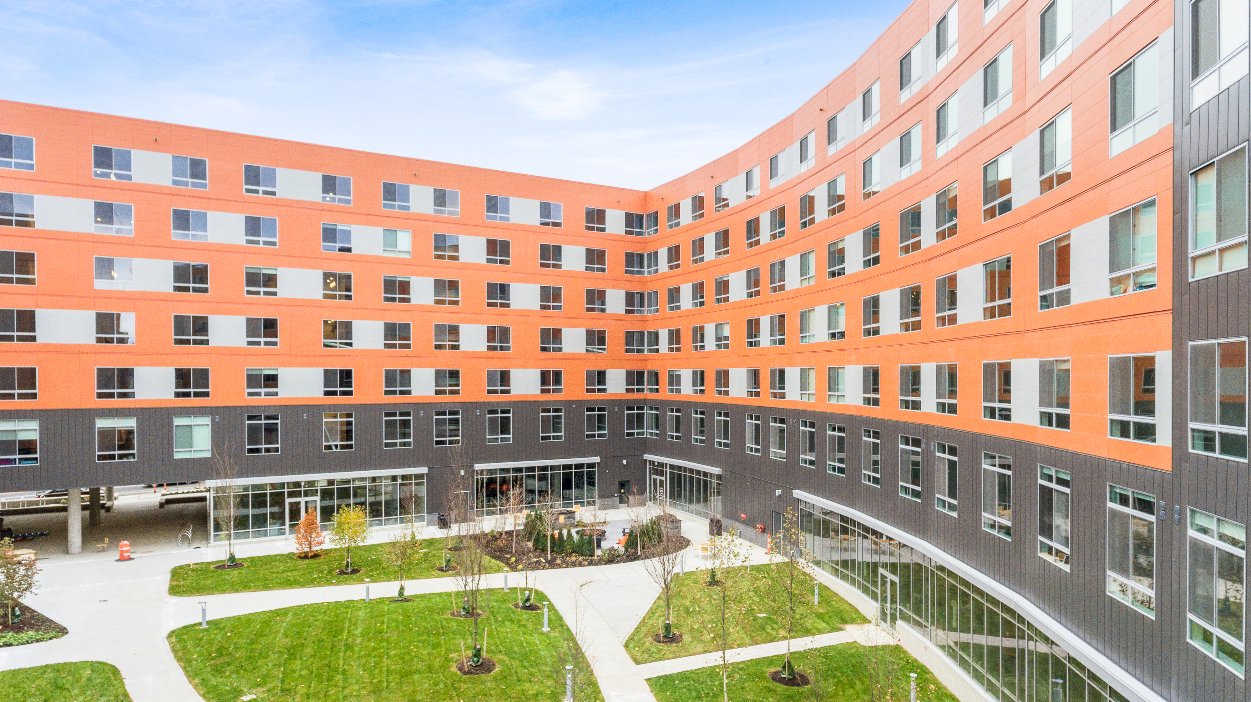 Exterior view of student housing with orange and gray exterior walls and a greenery-filled courtyard.