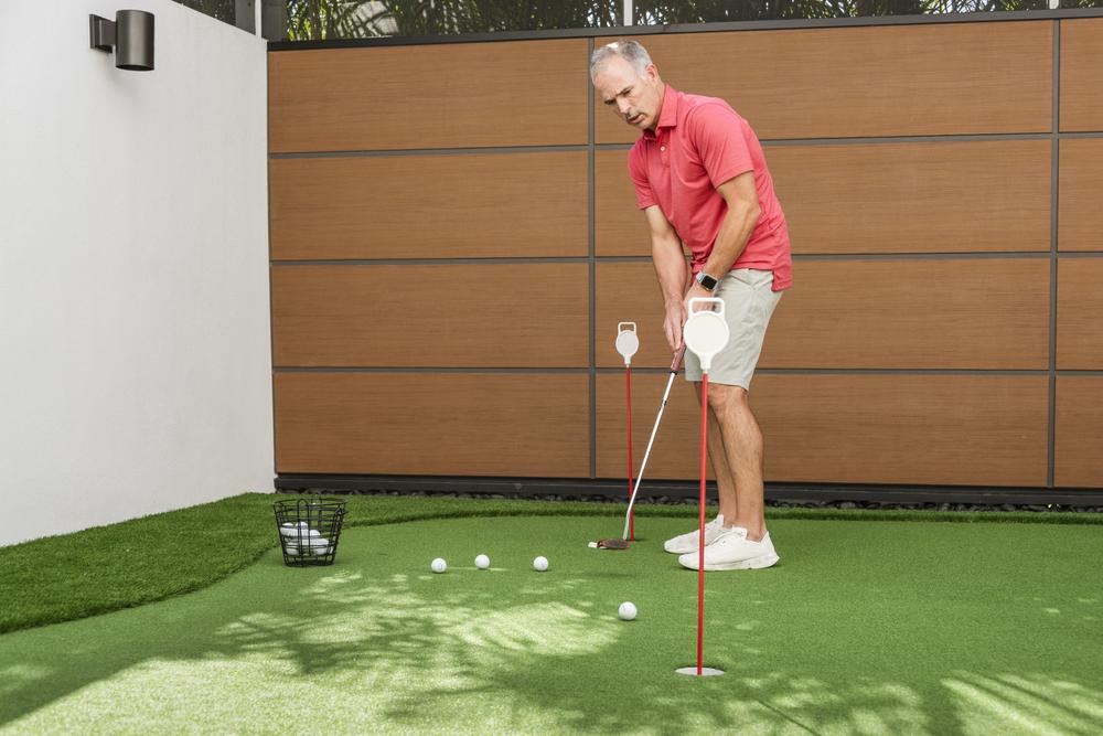 A man on a backyard golf green course hitting a golf ball in front of a wall utilizing Nichiha’s RiftSawn fiber cement cladding.
