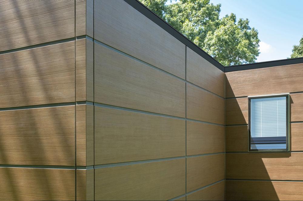 A close-up of Nichiha’s RiftSawn fiber cement cladding on a home with trees in the background.