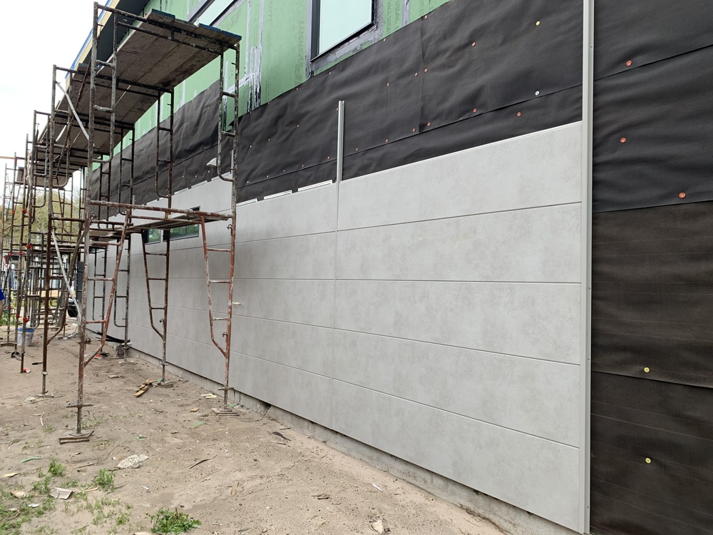 A wall under construction with light gray horizontal siding and a black rainscreen.