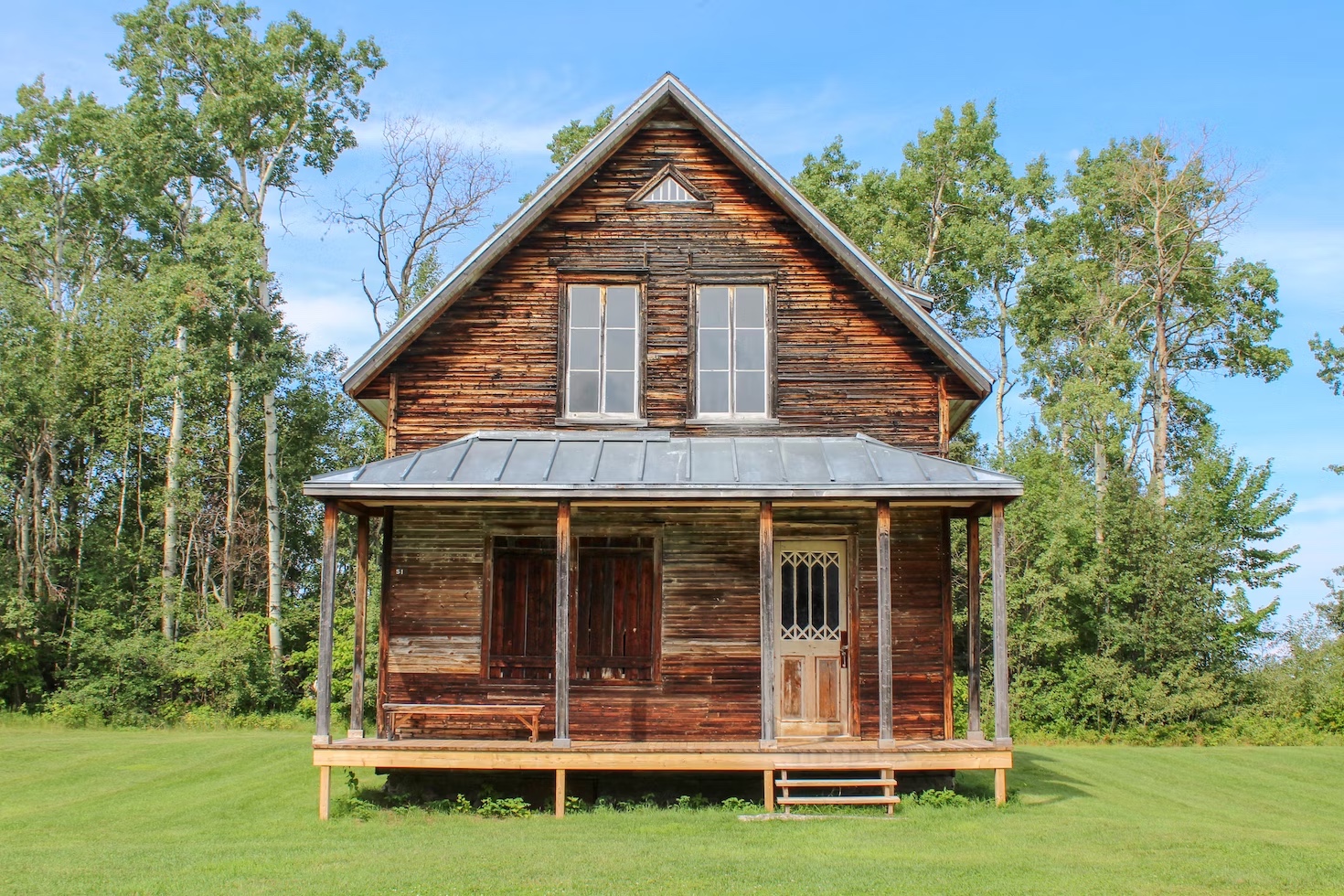 A two-story home with wood siding and a metal roof. The green backyard is lined with trees.