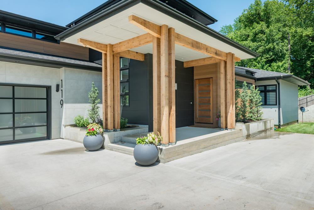 The front entryway of a home with a black wall design and wood-like accents. Two plants are on either side of the steps. 