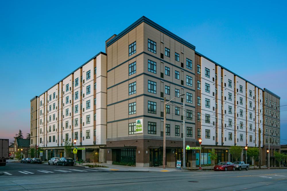This commercial building has apartments for lease. There are cars parked along the side of the building.