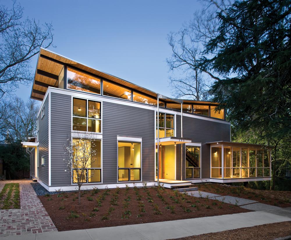 This two-story house has grey fiber-cement siding with warm interior lighting. There are small, freshly planted plants in the flower beds out front. 