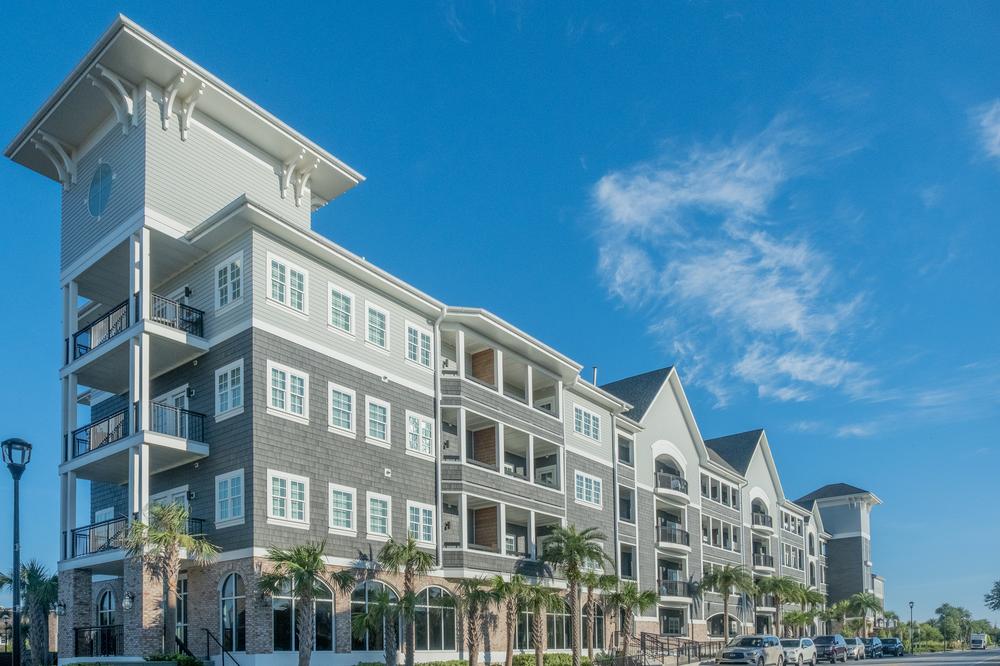 A street view of Henderson Beach Inn with gray shake siding and white trim. The perimeter is landscaped with palm trees.