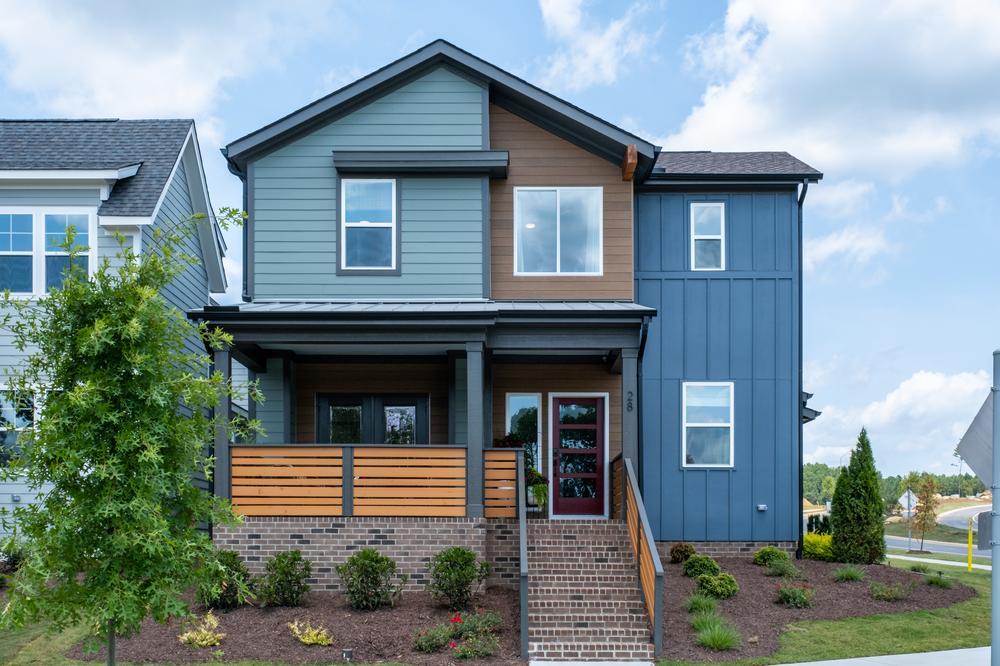 This two-story home has blue and wood-like siding. Brick steps lead up to the home’s front door and front porch.