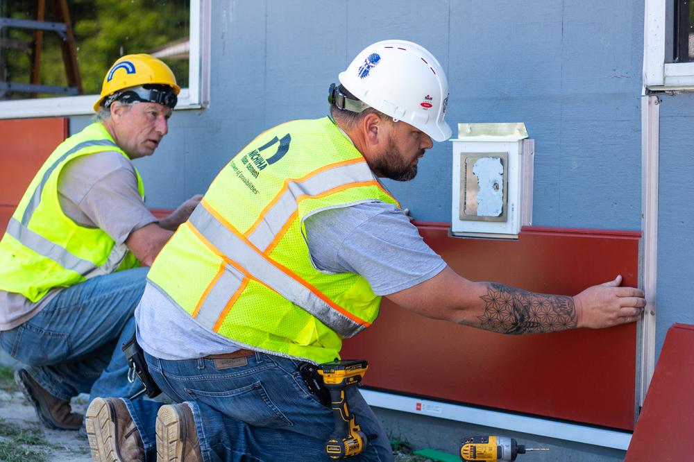Two people with yellow Nichiha vests installing Nichiha Illumination fiber cement panels.
