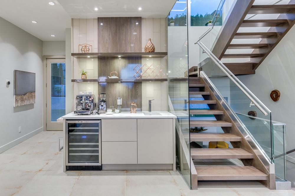 A home with a kitchen counter, shelves of decor and a staircase with glass siding.