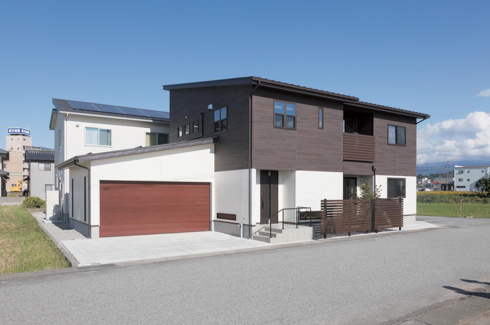 Nichiha’s fiber cement siding in white and dark brown on a home with a blue sky in the background and a large brownish-red garage door.