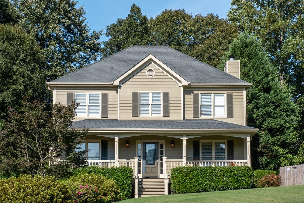 Two-story home with stairs leading up to a large front porch surrounded by green foliage.
