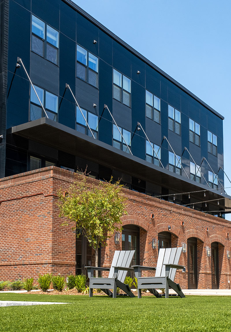 two lawn chairs sit in front of a mixed facade with red brick on lower half and black reflective miraia panels from nichiha